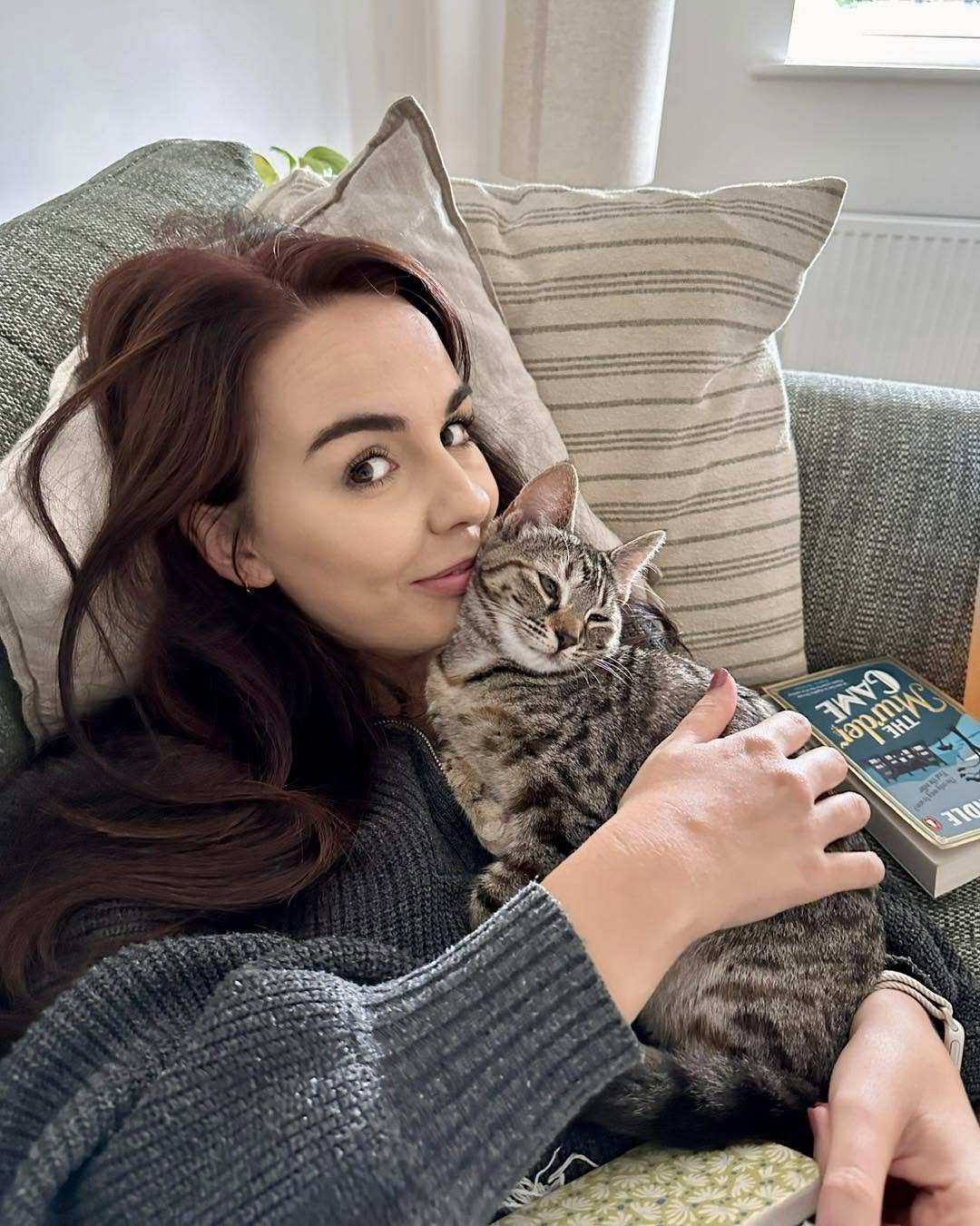 Jess cuddling a tabby cat on a green sofa