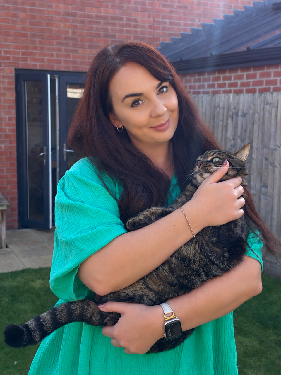 Jess holding a tabby cat in the garden
